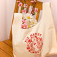 image of tote bag sitting on a chair  with flowers sticking out of the top. 
